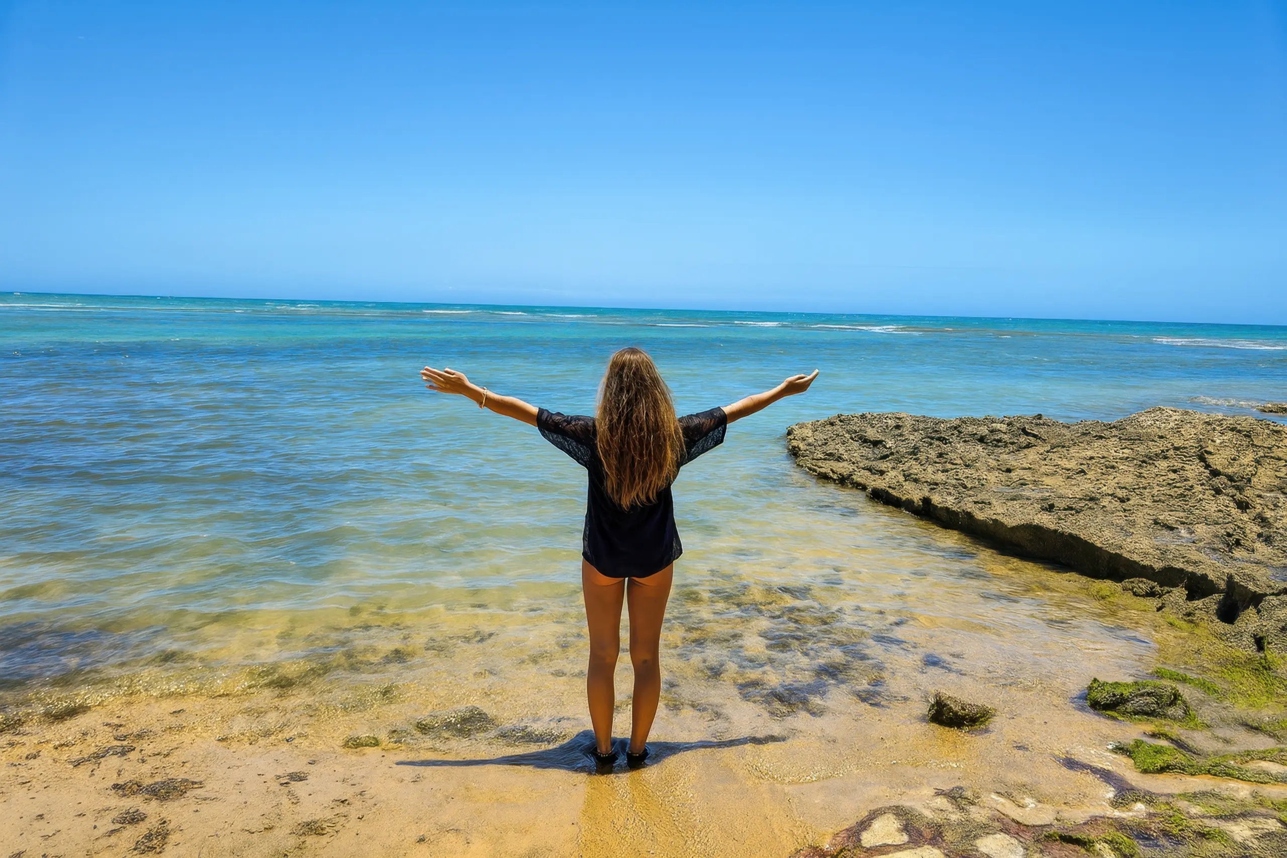 Mulher de costas com braços abertos em uma praia paradisíaca, simbolizando a liberdade dos passeios privativos.