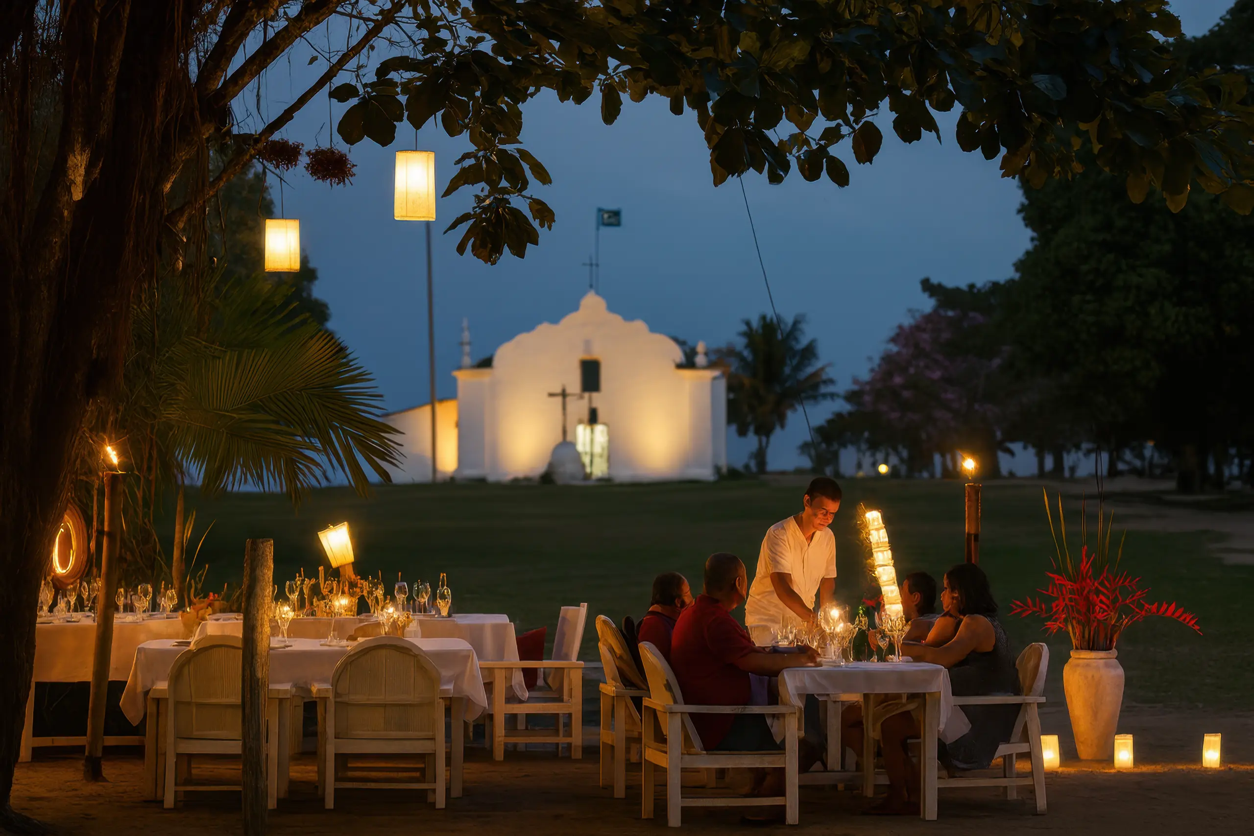 Jantar elegante ao ar livre no Quadrado de Trancoso, com mesas iluminadas por velas e a igreja ao fundo.