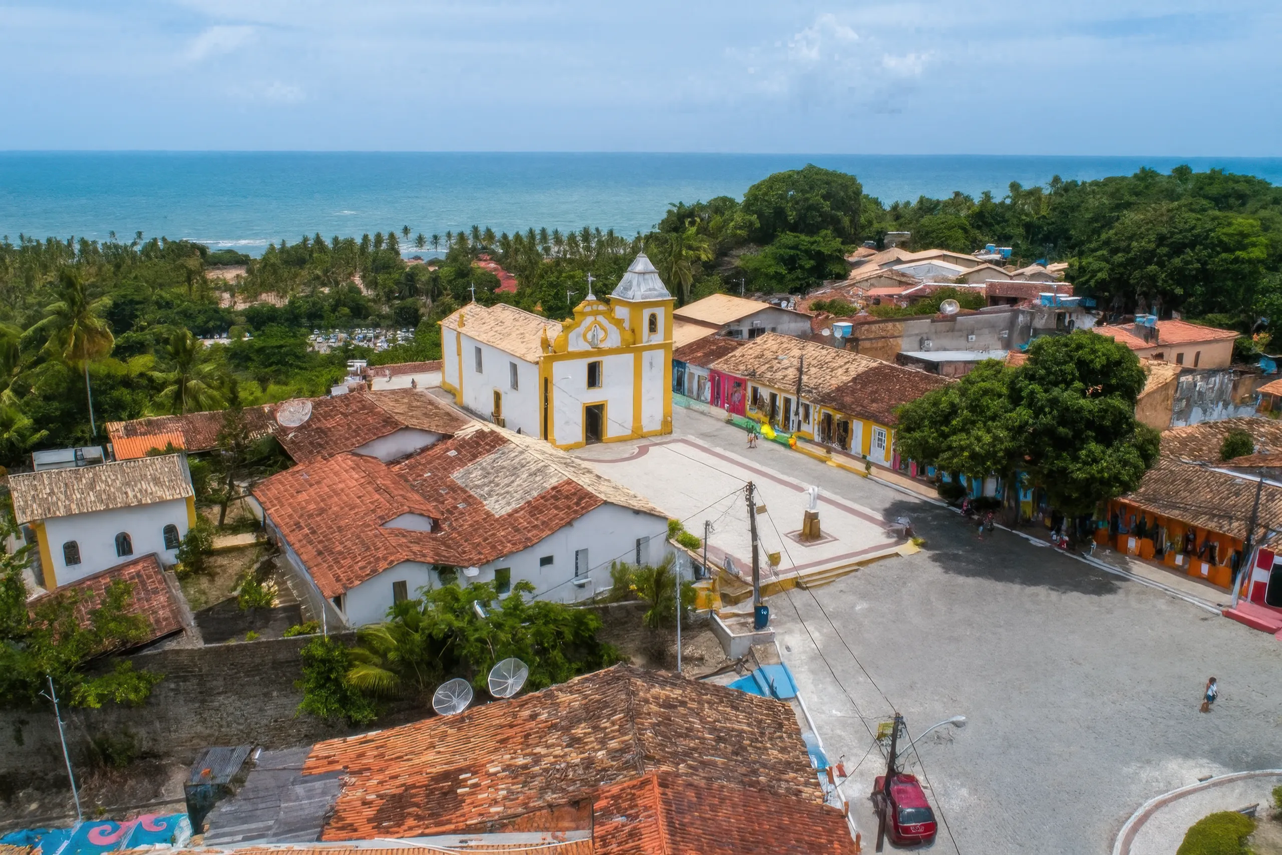 Vista aérea do charmoso centro histórico de Arraial d'Ajuda, com sua icônica igreja e casario colorido.