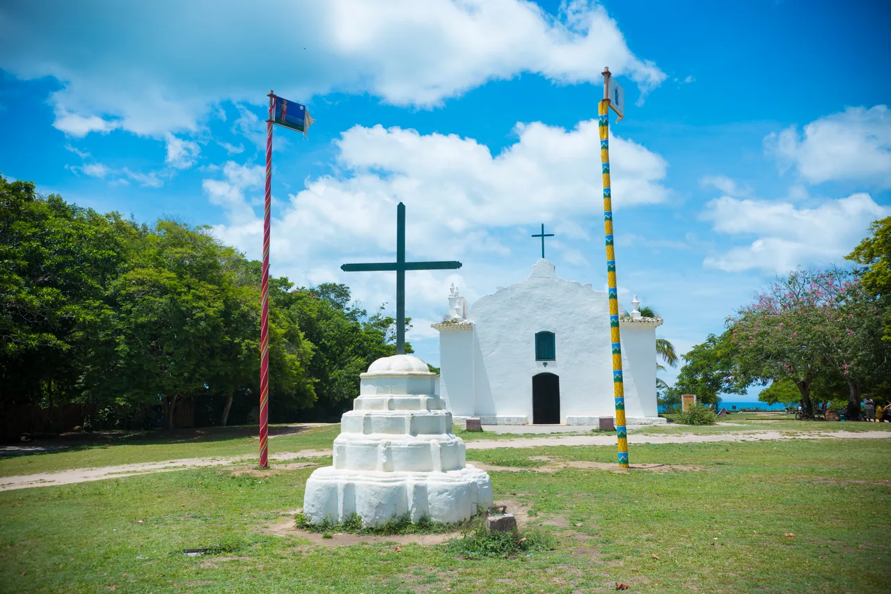 Igreja branca e gramado do Quadrado de Trancoso sob céu azul.